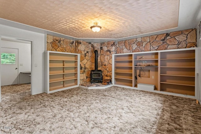 unfurnished living room with carpet, a wood stove, and a textured ceiling