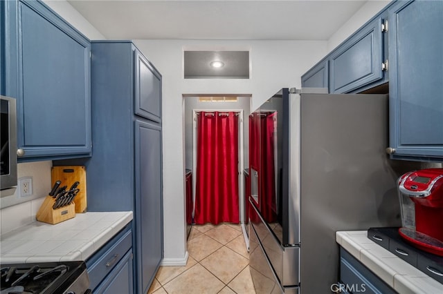 kitchen featuring light tile patterned flooring, tile countertops, stainless steel appliances, and blue cabinets