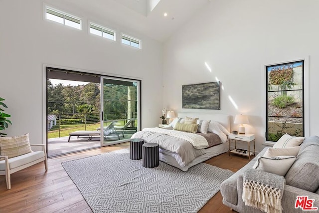 bedroom with hardwood / wood-style flooring, a towering ceiling, multiple windows, and access to exterior