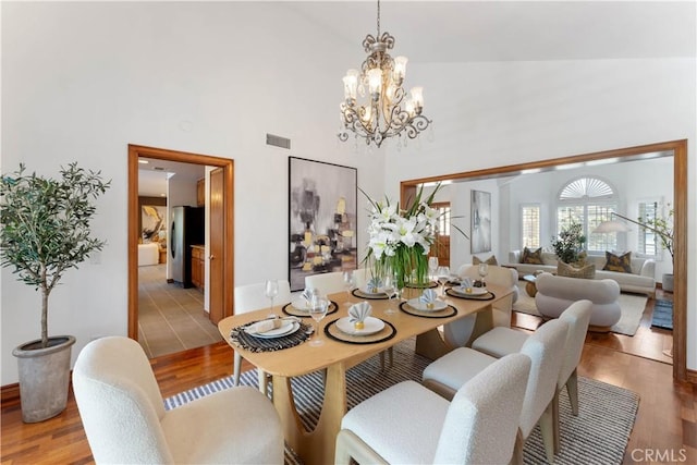 dining space with high vaulted ceiling, wood-type flooring, and an inviting chandelier