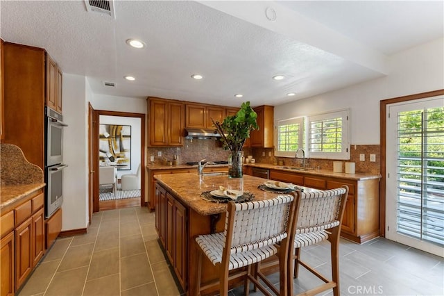 kitchen featuring sink, light stone countertops, an island with sink, and appliances with stainless steel finishes