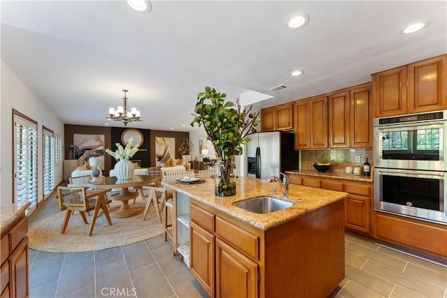 kitchen with sink, hanging light fixtures, an inviting chandelier, an island with sink, and appliances with stainless steel finishes