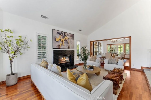 living room with hardwood / wood-style flooring, high vaulted ceiling, a brick fireplace, and a notable chandelier