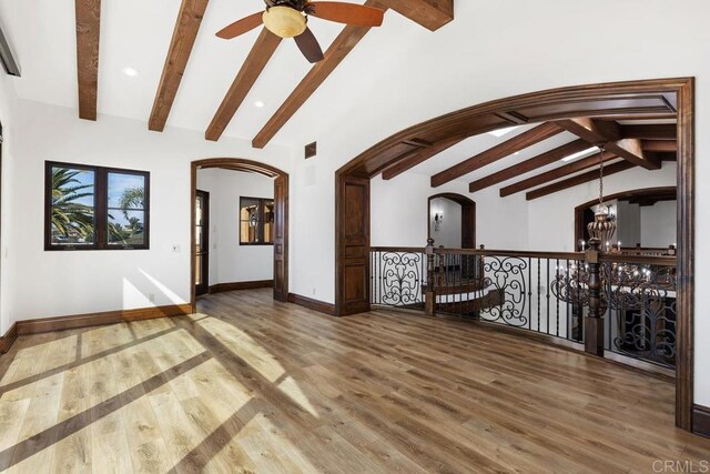 unfurnished room with ceiling fan with notable chandelier, wood-type flooring, and lofted ceiling with beams