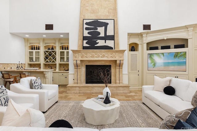 living room with a tile fireplace, a towering ceiling, bar, and built in features