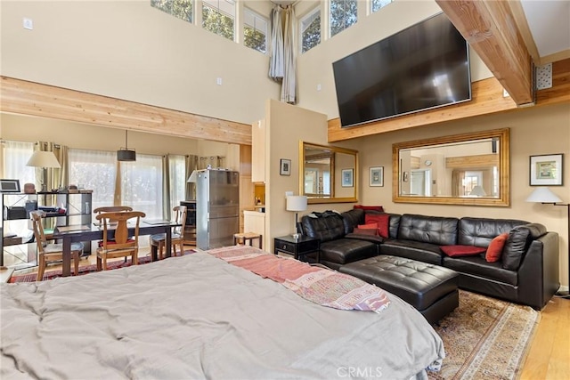 bedroom featuring beamed ceiling, stainless steel fridge, light wood-type flooring, and multiple windows