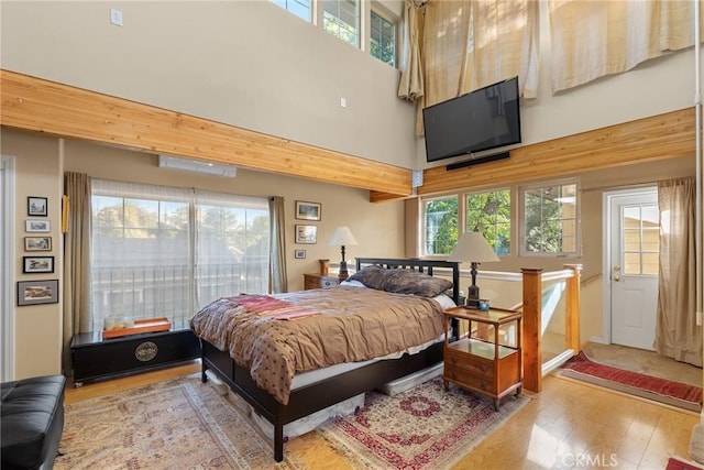 bedroom with multiple windows, light hardwood / wood-style floors, and a high ceiling