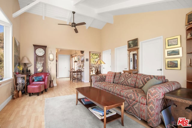 living room featuring ceiling fan, light wood-type flooring, a wealth of natural light, and beamed ceiling