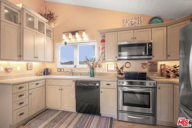 kitchen featuring appliances with stainless steel finishes, lofted ceiling, cream cabinetry, and sink