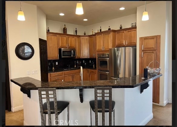 kitchen featuring a breakfast bar, pendant lighting, stainless steel appliances, and a center island with sink