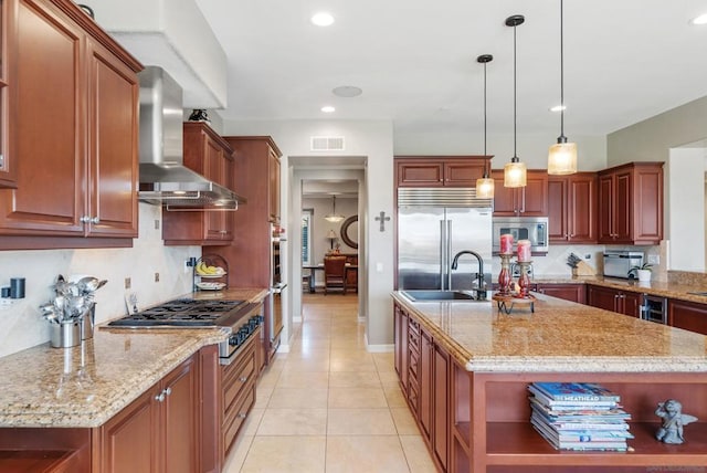 kitchen with built in appliances, a kitchen island with sink, wall chimney exhaust hood, and light stone countertops