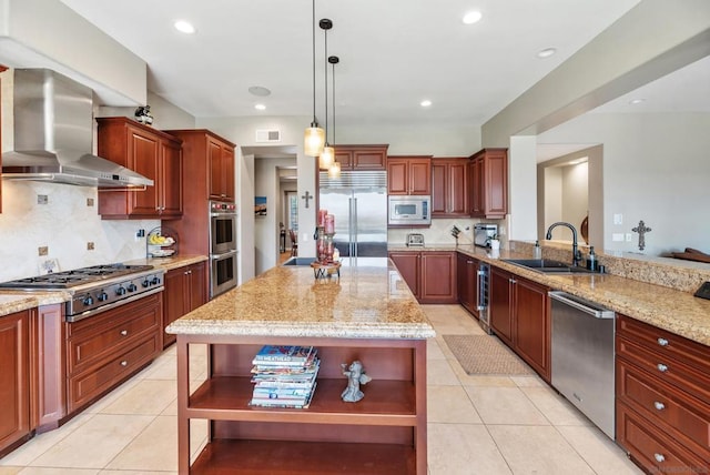 kitchen featuring wall chimney range hood, sink, built in appliances, light stone countertops, and decorative light fixtures