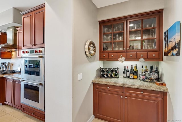 kitchen featuring light stone counters, white double oven, light tile patterned floors, and stainless steel gas stovetop