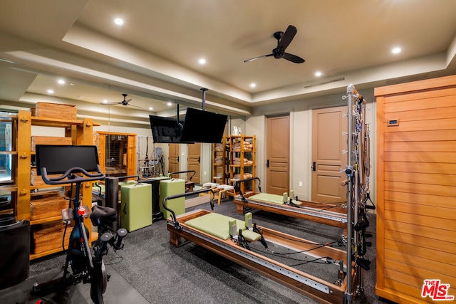 exercise room featuring carpet flooring, ceiling fan, and a raised ceiling