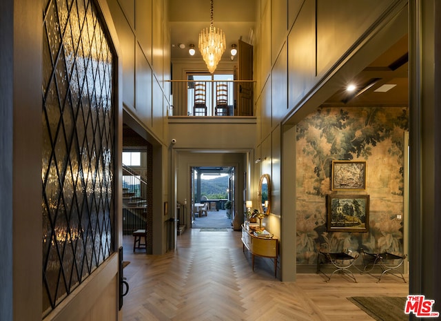 foyer featuring a towering ceiling, parquet floors, and a chandelier