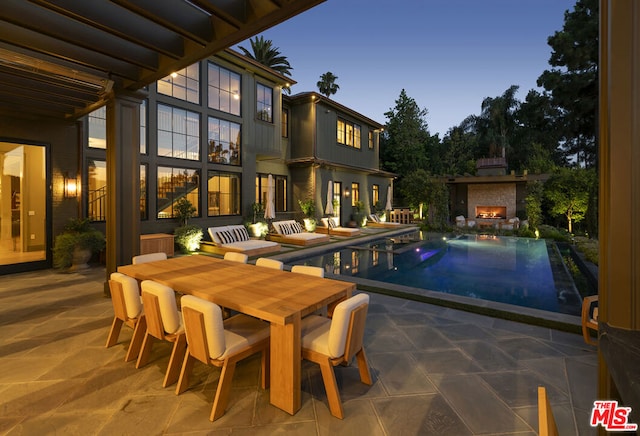 pool at dusk with an outdoor fireplace and a patio