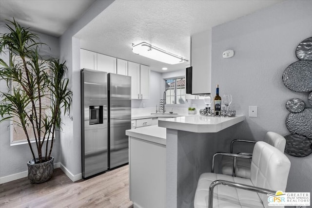 kitchen with white cabinets, kitchen peninsula, stainless steel fridge with ice dispenser, light wood-type flooring, and a kitchen bar