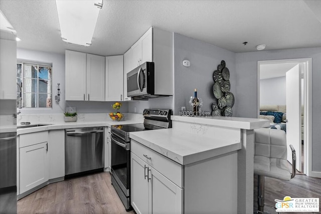 kitchen with appliances with stainless steel finishes, kitchen peninsula, white cabinetry, and light hardwood / wood-style floors