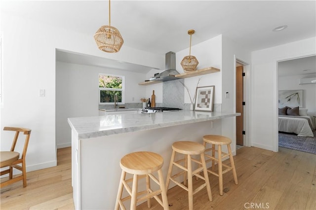 kitchen with kitchen peninsula, light hardwood / wood-style floors, a breakfast bar area, and wall chimney range hood