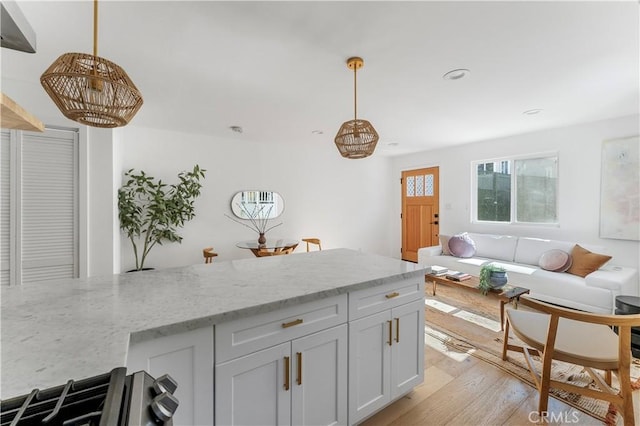 kitchen featuring pendant lighting, light stone countertops, light wood-type flooring, and stainless steel stove