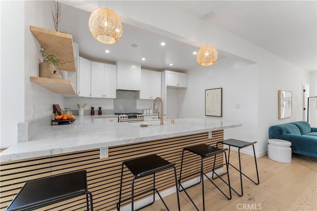 kitchen with white cabinetry, premium range hood, kitchen peninsula, a breakfast bar area, and light wood-type flooring