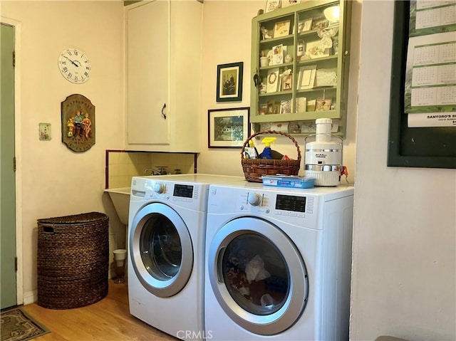 laundry room with washer and clothes dryer, light hardwood / wood-style floors, and cabinets