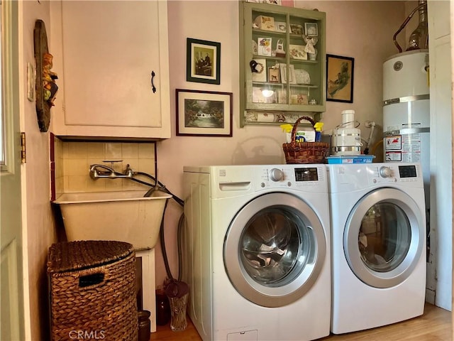 laundry room with cabinets, sink, light hardwood / wood-style flooring, washer and dryer, and strapped water heater