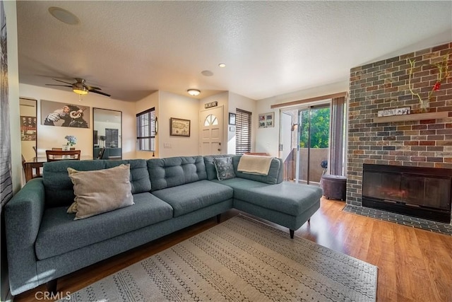 living room with ceiling fan, a fireplace, wood-type flooring, and a textured ceiling