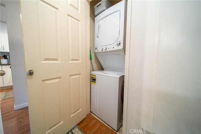 laundry room featuring stacked washing maching and dryer and light hardwood / wood-style floors