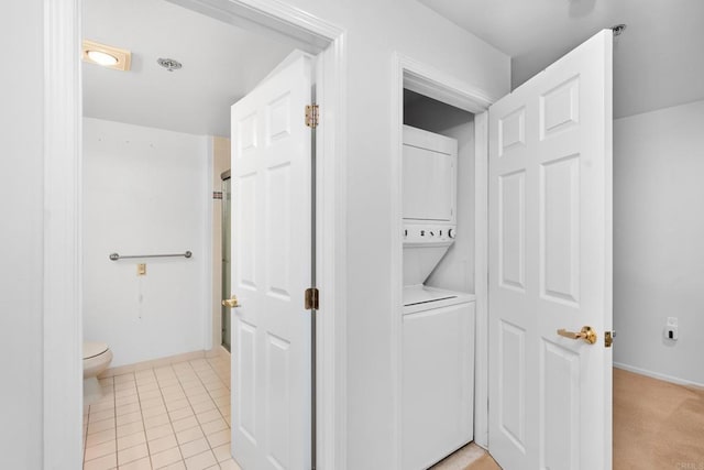 laundry area featuring light tile patterned flooring, stacked washer and clothes dryer, baseboards, and laundry area