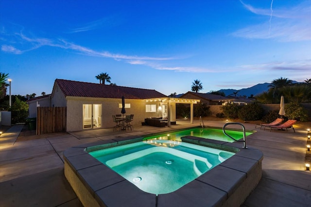 pool at dusk with an in ground hot tub, a mountain view, and a patio