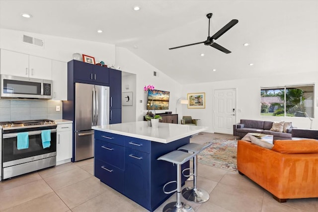 kitchen with white cabinets, blue cabinets, vaulted ceiling, appliances with stainless steel finishes, and a kitchen island