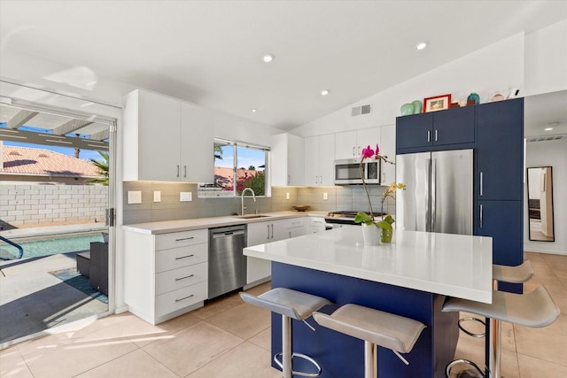 kitchen with vaulted ceiling, light tile patterned floors, a kitchen island, white cabinetry, and stainless steel appliances