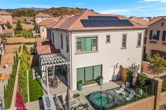 back of house featuring solar panels, a patio area, a mountain view, and an in ground hot tub