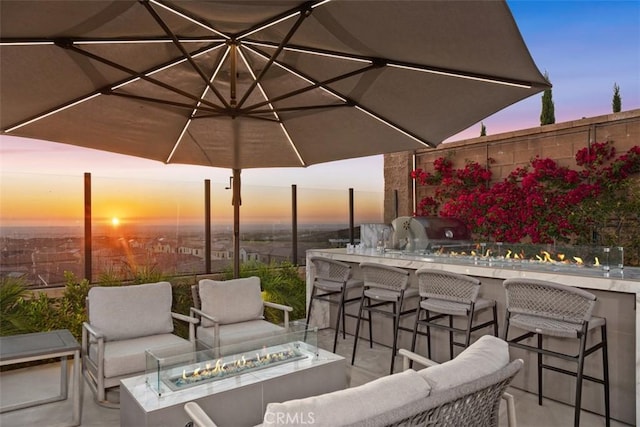 patio terrace at dusk featuring an outdoor living space with a fire pit, a grill, and an outdoor bar