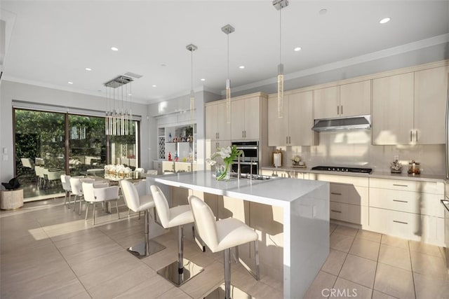 kitchen with a breakfast bar, a center island with sink, sink, hanging light fixtures, and light tile patterned floors