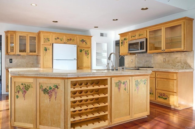 kitchen featuring white refrigerator, decorative backsplash, dark hardwood / wood-style floors, and a center island with sink