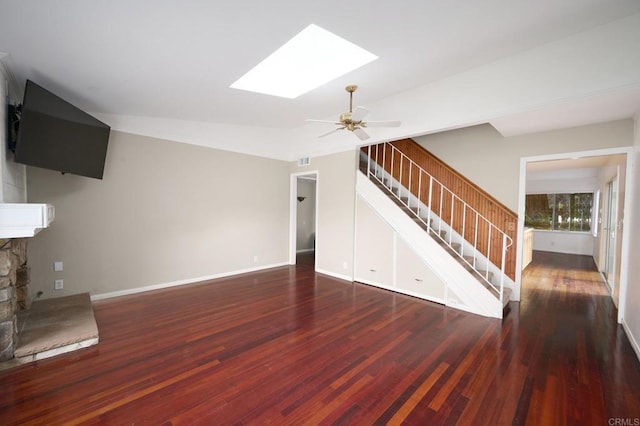 unfurnished living room featuring a fireplace, dark wood-type flooring, vaulted ceiling with skylight, and ceiling fan