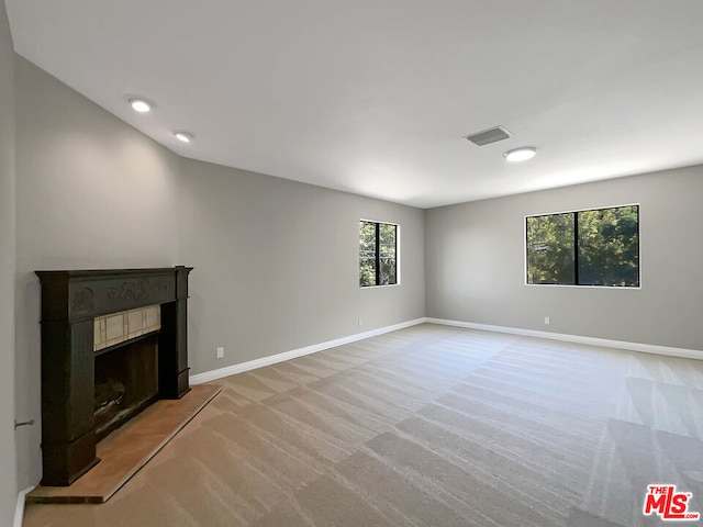 unfurnished living room with a tiled fireplace, vaulted ceiling, and light colored carpet