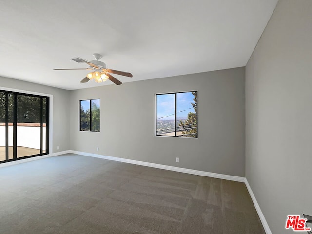 empty room with dark carpet, ceiling fan, and a healthy amount of sunlight