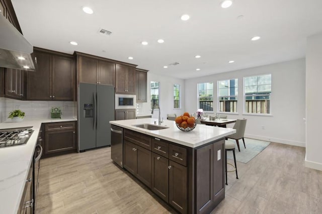 kitchen with light hardwood / wood-style floors, a kitchen island with sink, range hood, sink, and appliances with stainless steel finishes