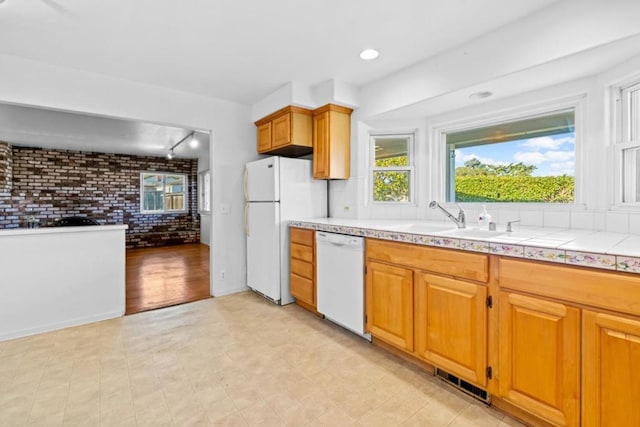 kitchen with brick wall, tile countertops, sink, track lighting, and white appliances