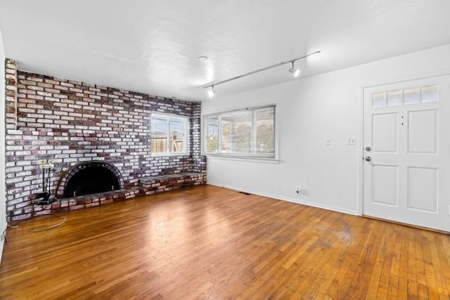 unfurnished living room with hardwood / wood-style flooring, brick wall, track lighting, and a fireplace