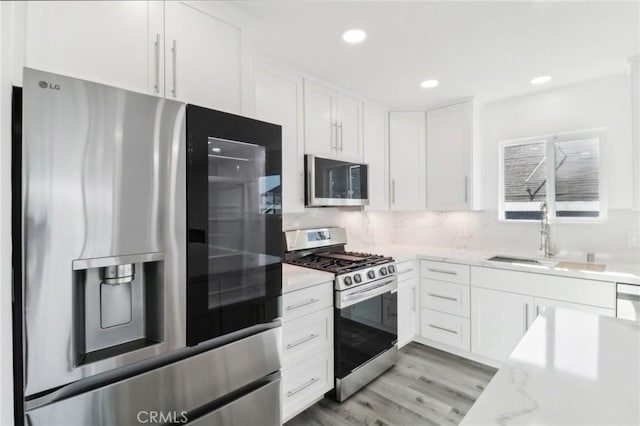 kitchen with white cabinetry, appliances with stainless steel finishes, light hardwood / wood-style flooring, light stone counters, and sink