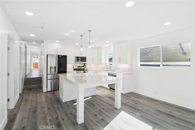 kitchen with stainless steel appliances, white cabinets, a center island, and decorative light fixtures