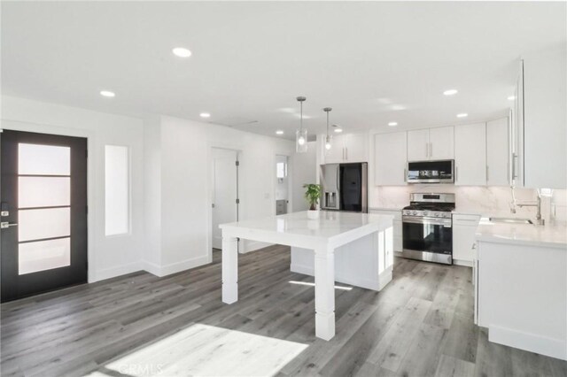 kitchen with a kitchen island, pendant lighting, sink, appliances with stainless steel finishes, and white cabinets