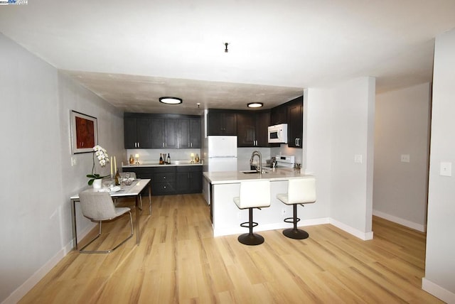 kitchen featuring kitchen peninsula, a kitchen breakfast bar, white appliances, and light hardwood / wood-style floors