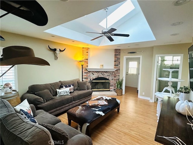 living room featuring a brick fireplace, a skylight, light hardwood / wood-style flooring, and a healthy amount of sunlight