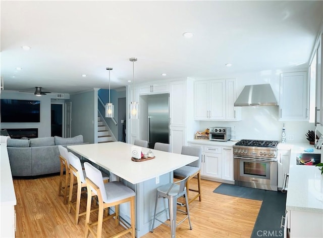 kitchen featuring premium appliances, wall chimney range hood, decorative light fixtures, light hardwood / wood-style flooring, and white cabinets