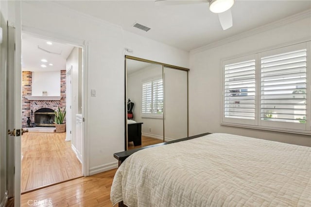 bedroom with ceiling fan, crown molding, a closet, a fireplace, and hardwood / wood-style flooring